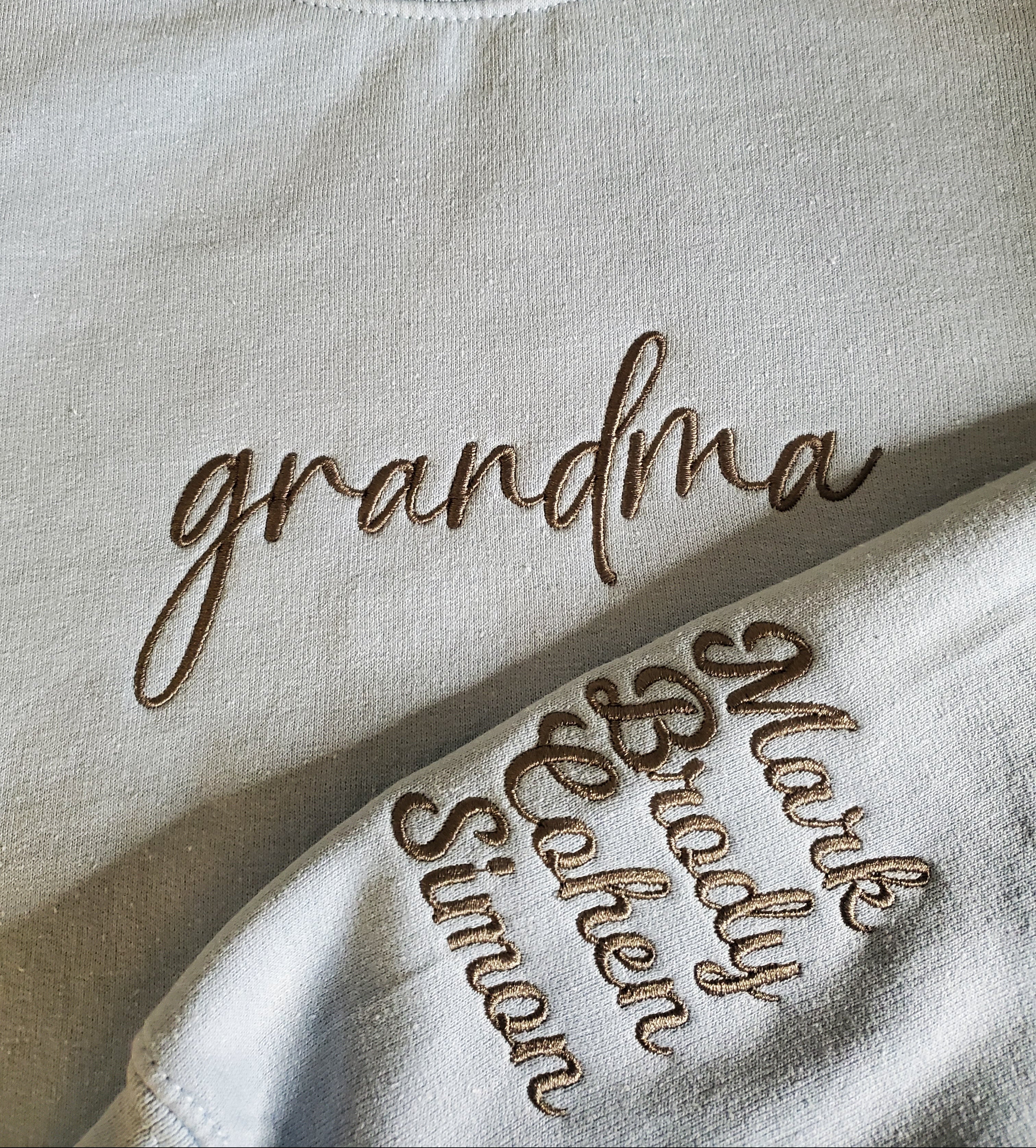 Beige sweatshirt with embroidered text on a plain background