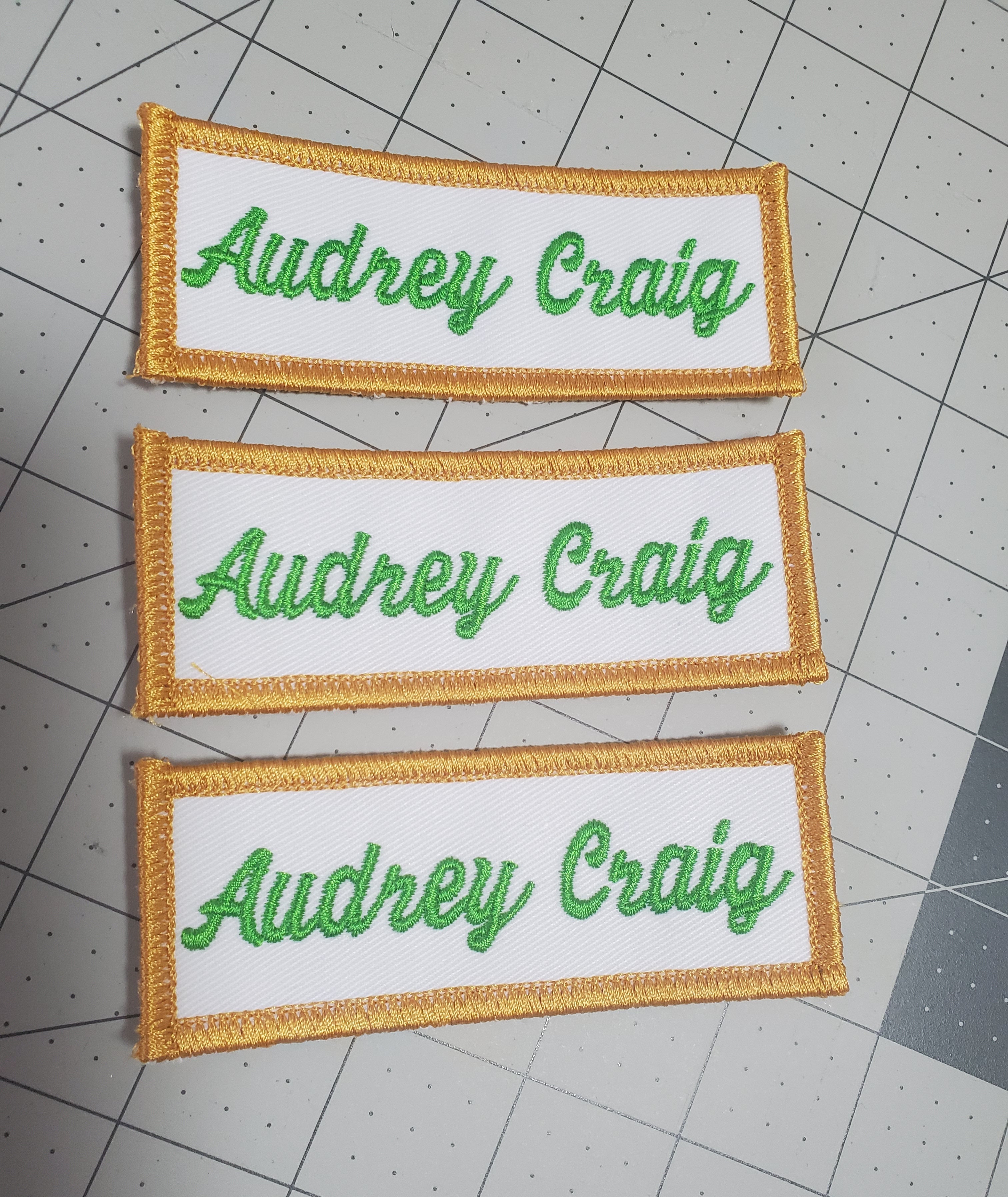 Three embroidered patches with 'Audrey Craig' text on a grid background