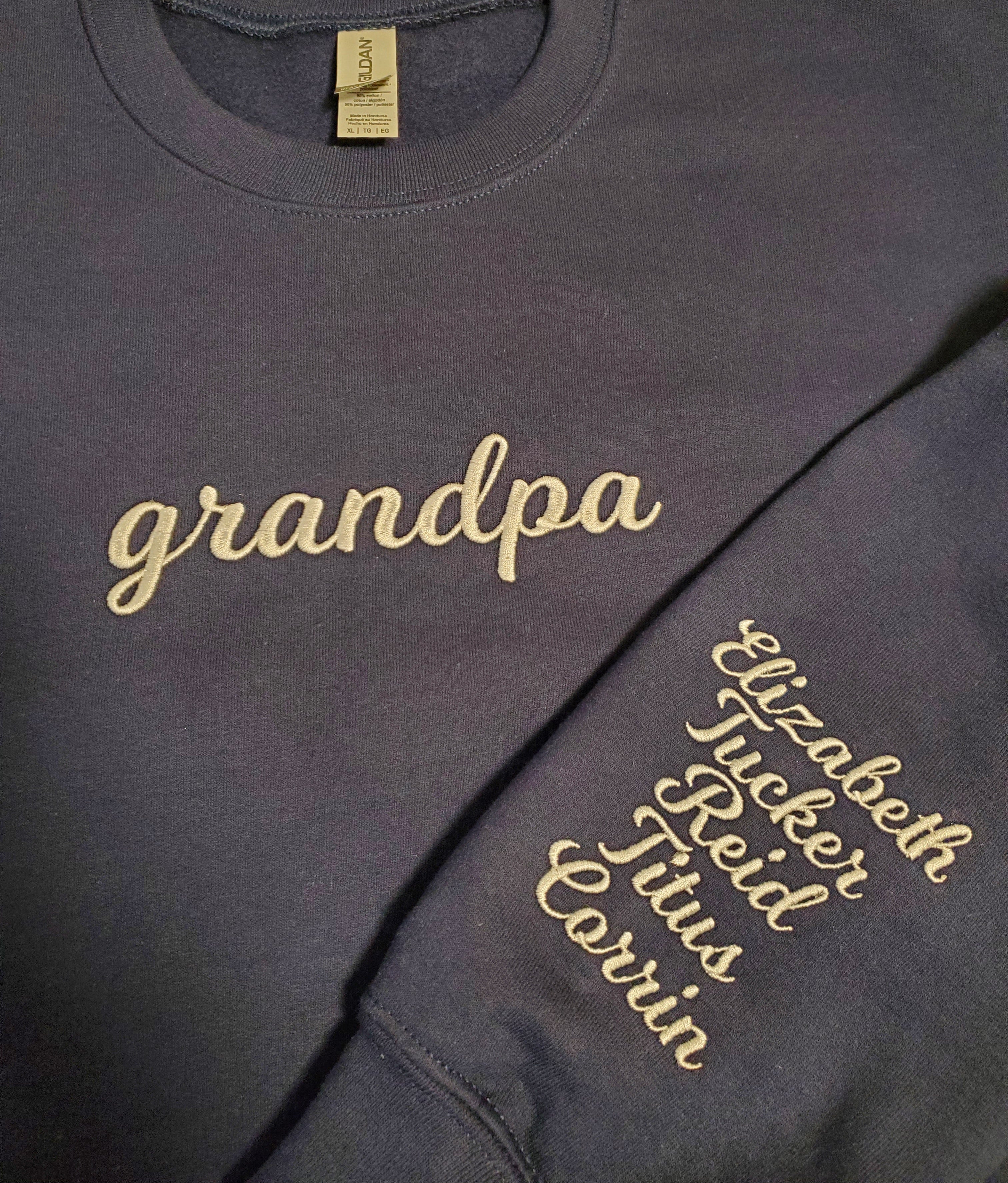 Navy sweatshirt with 'grandpa' and other text in gold on a tiled floor background